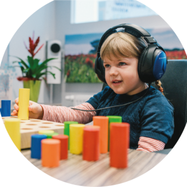 Ein Kind trägt große Kopfhörer und spielt mit Bausteinen im Rahmen der Pädakustik bei Hörgeräte Jens Steudler