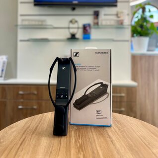 Ein schwarzes Gerät zum Kabellosen Hören beim Fernsehen der Marke Sennheiser steht auf einem Tisch neben seiner Verpackungsbox. Der Name des Modells ist: "Set 860".